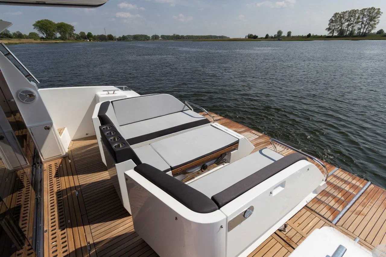 Outdoor lounge area on a boat features cushioned seating, cup holders, and a scenic view of the water and shoreline.