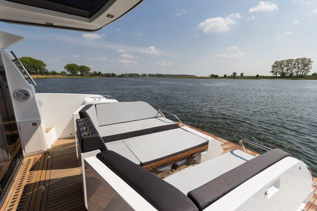 Luxurious boat deck with gray seating, cup holders, and scenic view of calm water and trees under a clear blue sky.