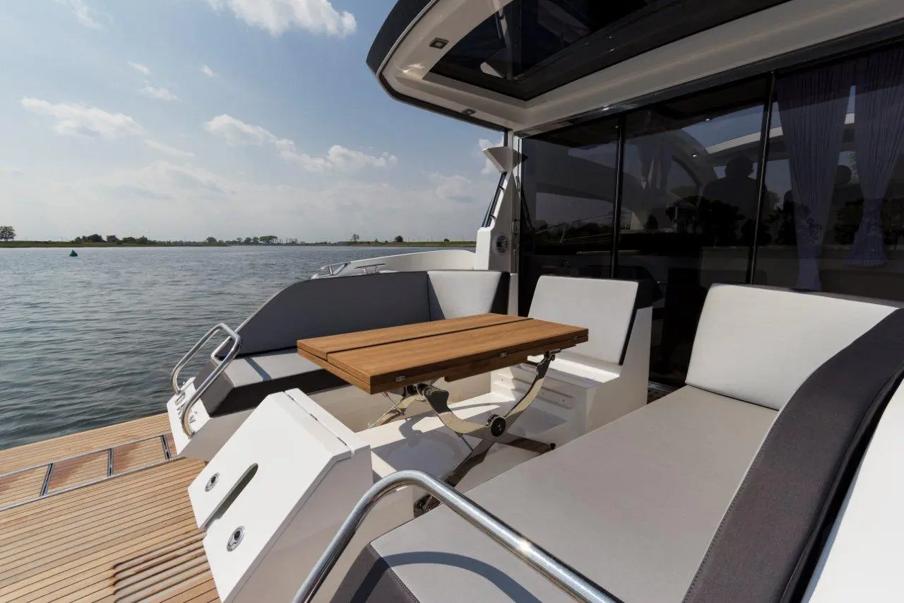 Luxury yacht deck with a wooden table, gray seating, and a scenic waterfront view under a clear sky.