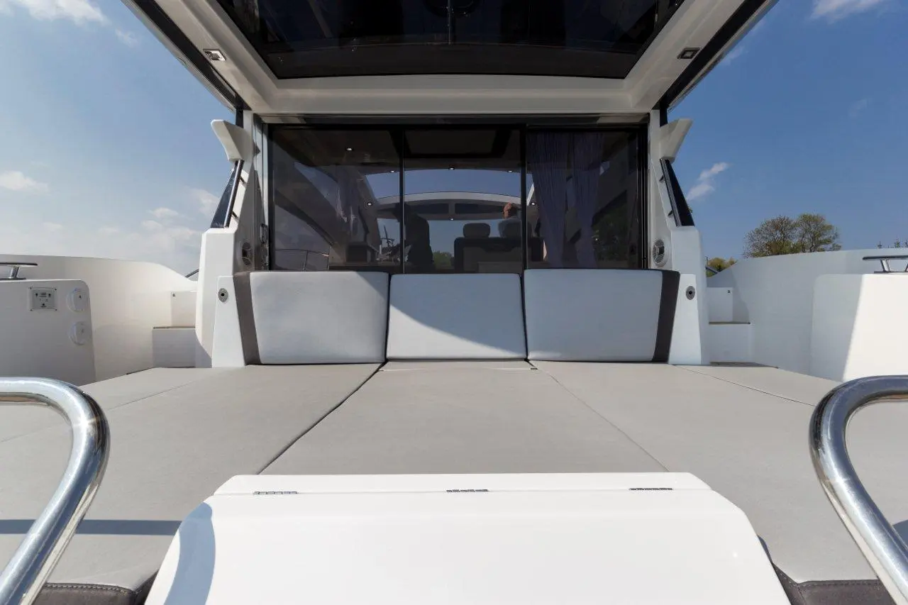 Interior view of a modern yacht, featuring gray cushions on a deck, clear windows, and a blue sky outside.