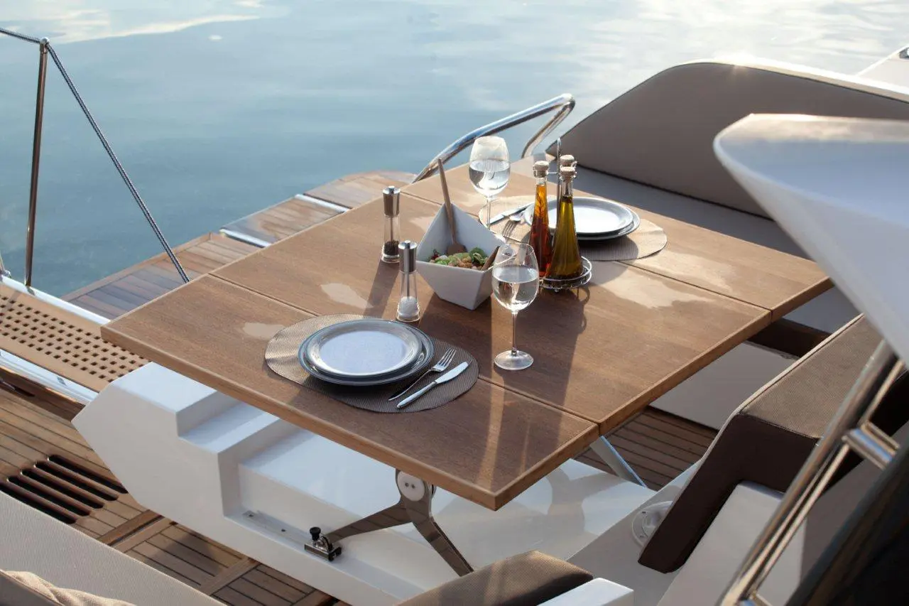 Elegant table set for dining on a yacht, featuring salad, glasses of water, and olive oil in the background.