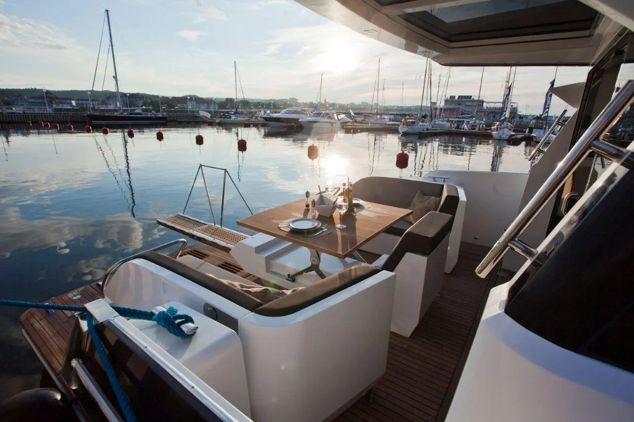 Luxury yacht deck with a dining table set for two, overlooking a marina at sunset with reflections on calm water.