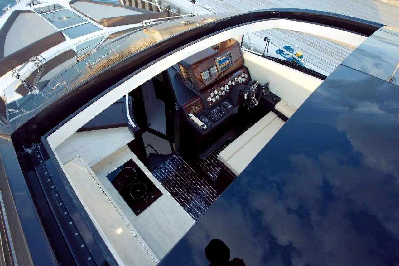 Interior view of a luxury yacht cockpit showing controls, steering wheel, and stovetop, with wooden and black finishes.
