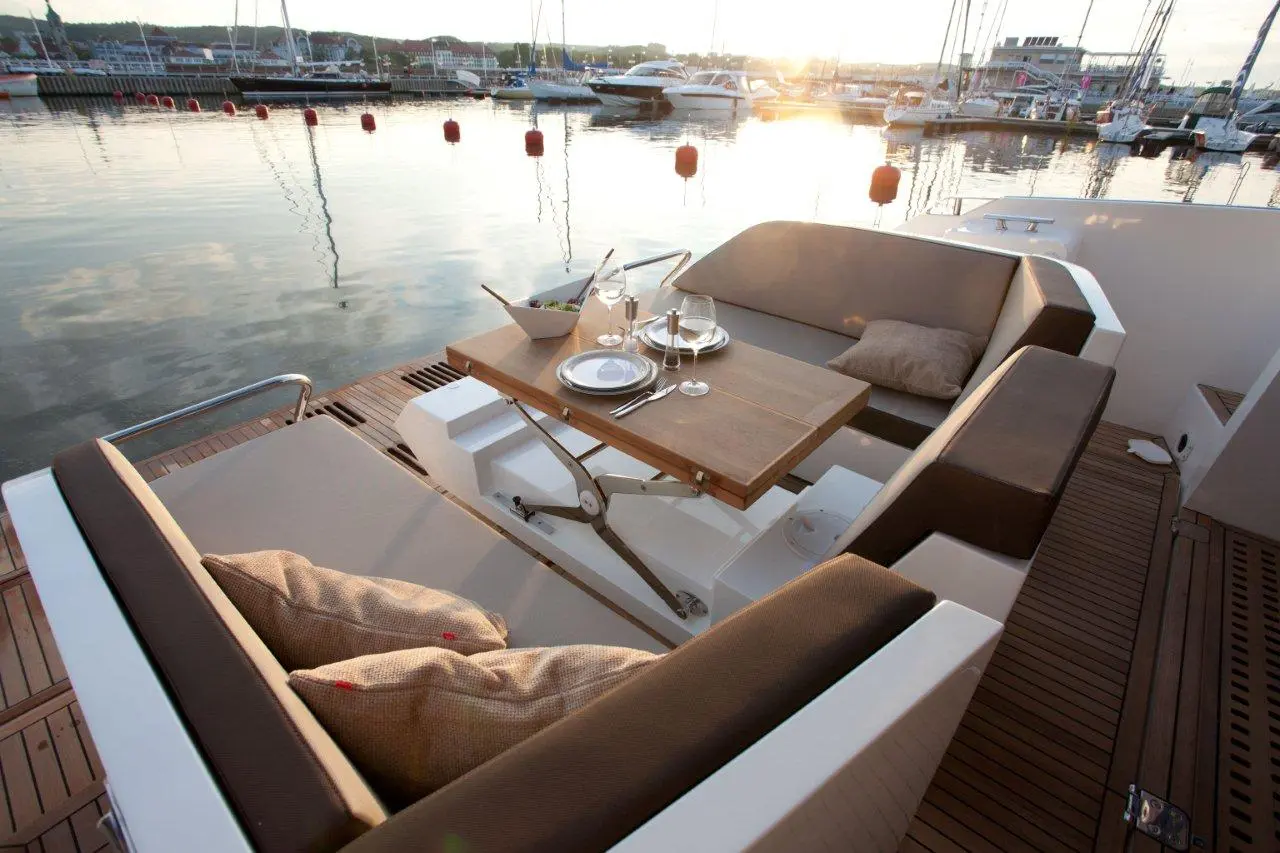 Luxurious boat seating area with a table set for a meal, overlooking a tranquil marina at sunset.