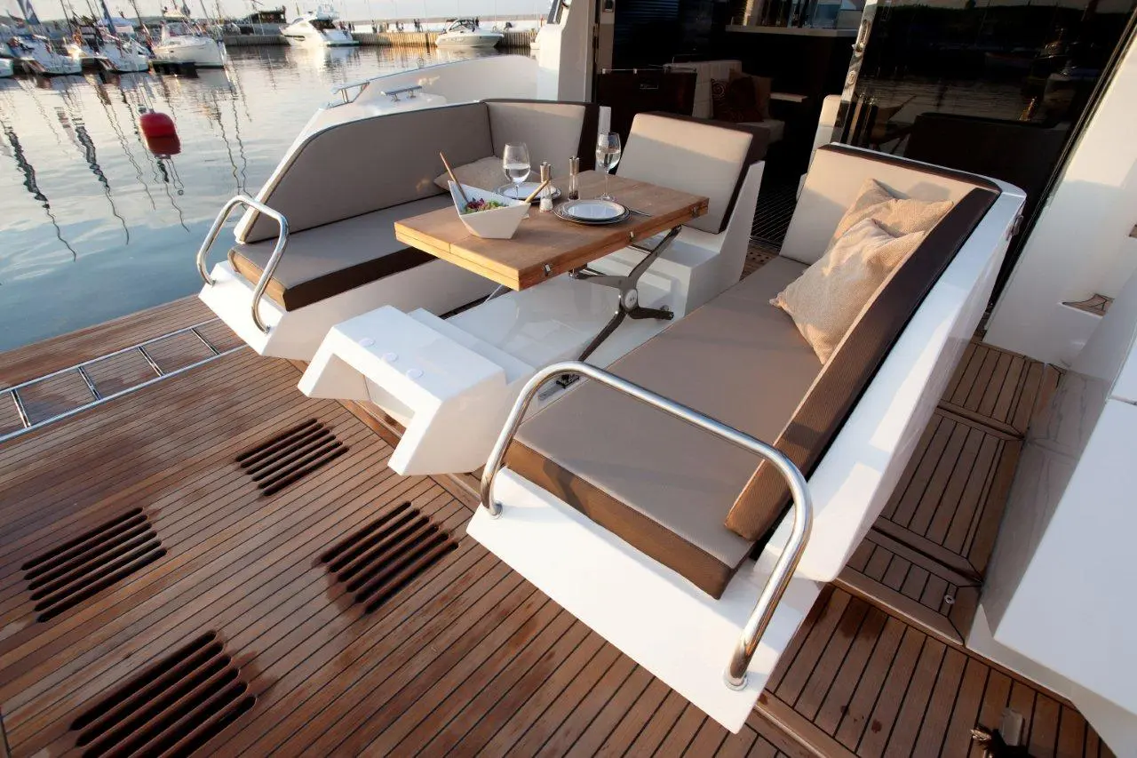Luxury yacht deck with two modern seating areas and a wooden table set for dining, overlooking the marina and calm waters.