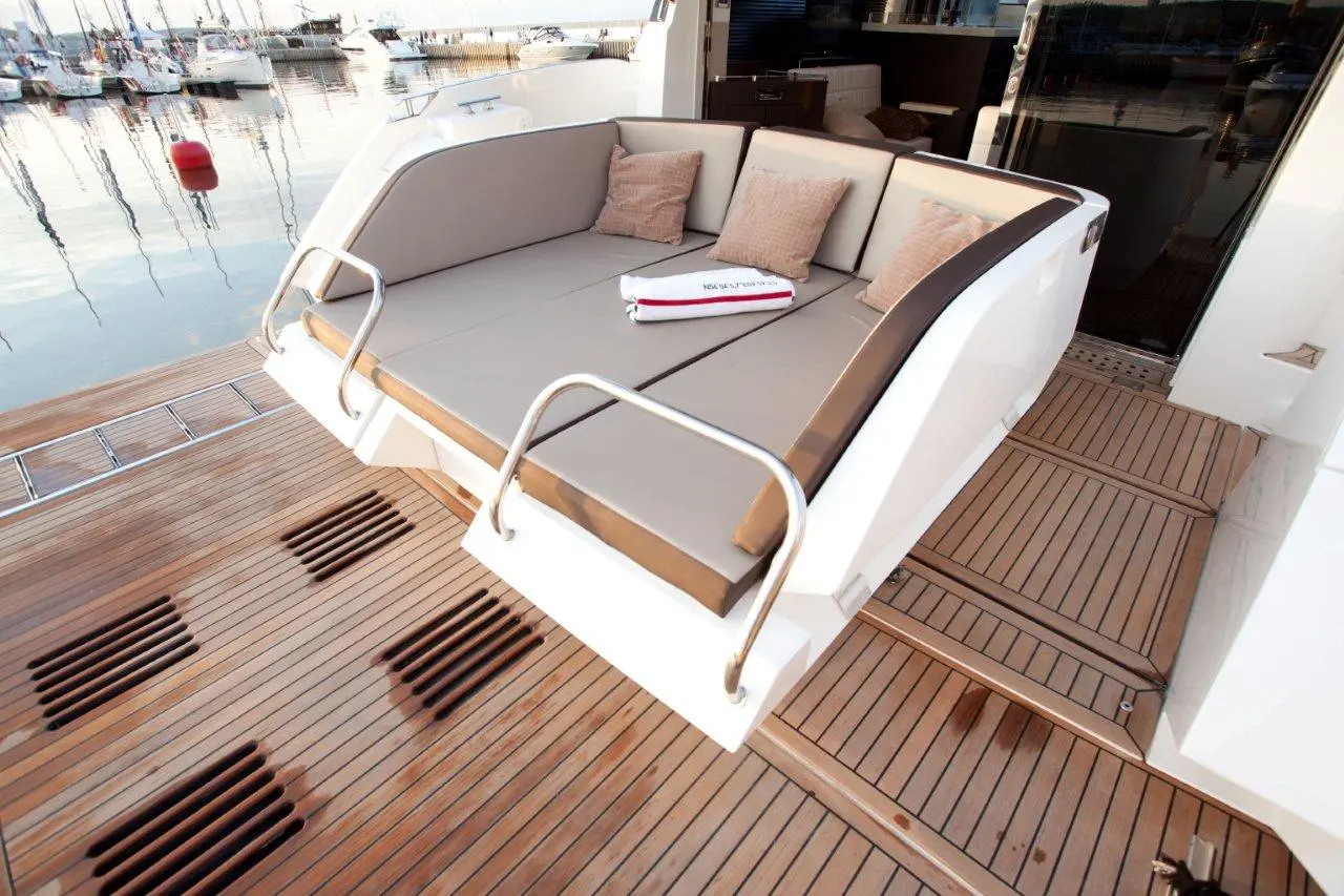A luxury yacht's outdoor seating area with plush cushions and a towel, overlooking calm harbor waters and moored boats.