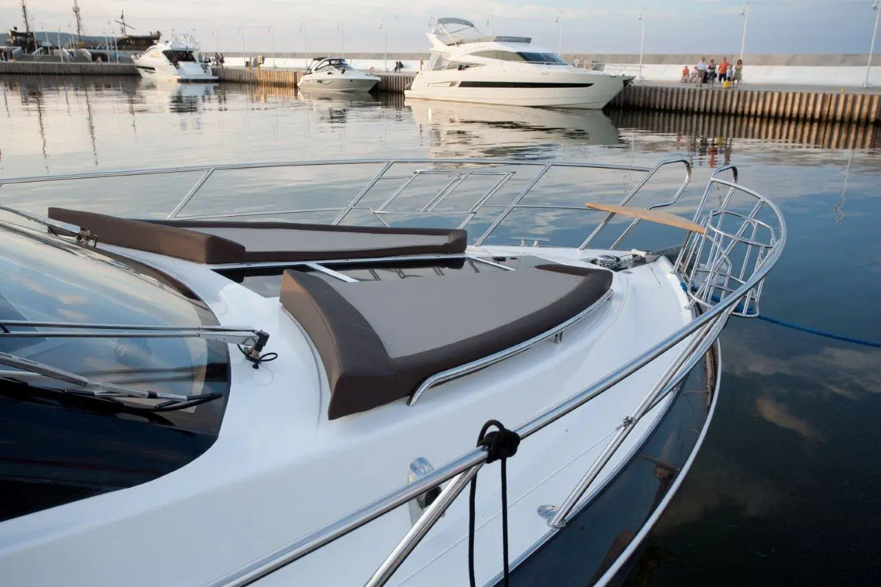 A luxury motorboat with cushioned sunbeds moored at a peaceful marina, reflecting calm waters and cloudy skies.