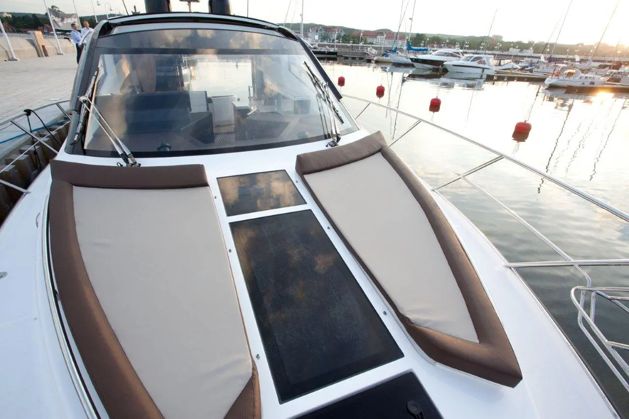 Luxury yacht deck with cushioned seating, overlooking a marina filled with boats and calm water at sunset.
