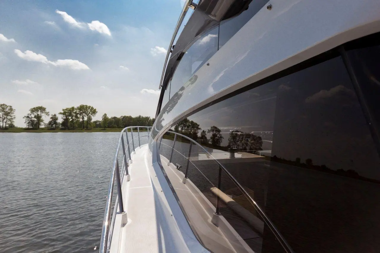 View of a luxury yacht's deck reflecting sunlight on calm waters, surrounded by lush greenery under a clear blue sky.