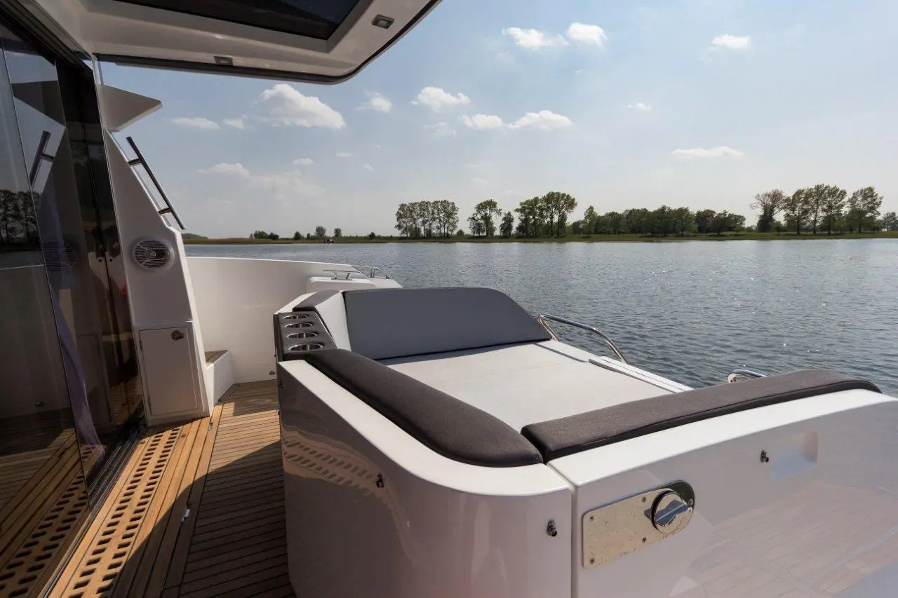 Luxurious boat deck featuring a sun lounger, wooden flooring, and serene water view with distant trees under a clear sky.