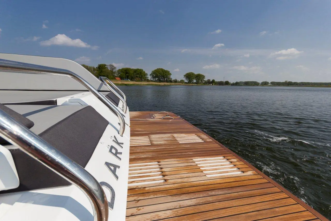 A motorboat is docked on a wooden jetty by the lake, surrounded by trees under a clear blue sky.