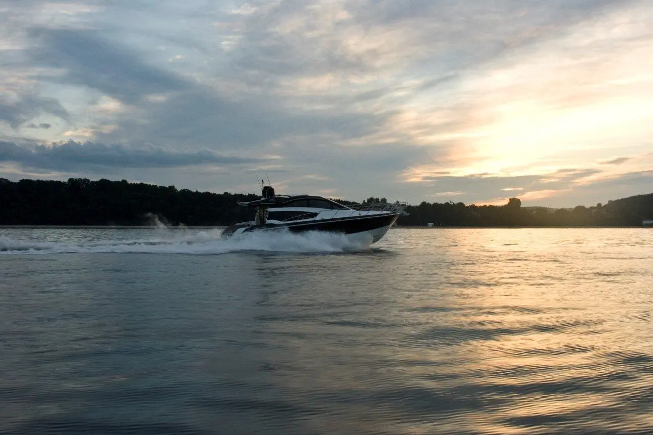 A sleek motorboat speeds across a calm lake at sunset, creating waves in the shimmering water.