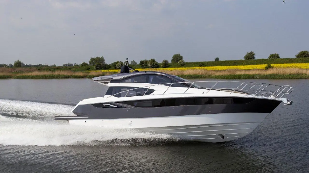 A sleek motor yacht speeds through calm waters, surrounded by lush green banks and a bright blue sky.