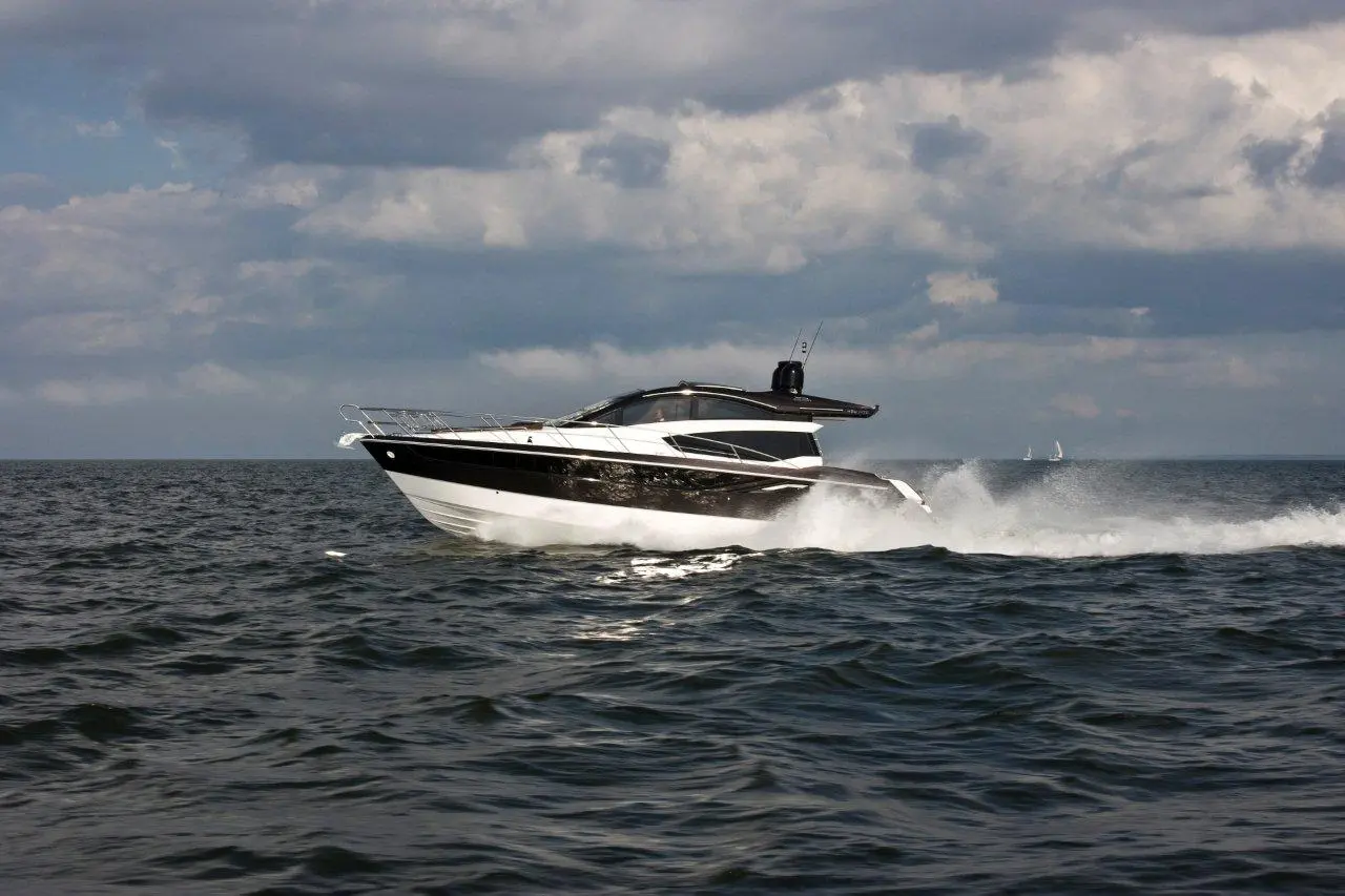 A sleek black and white motorboat gliding through dark waters, leaving a trail of foam under a cloudy sky.