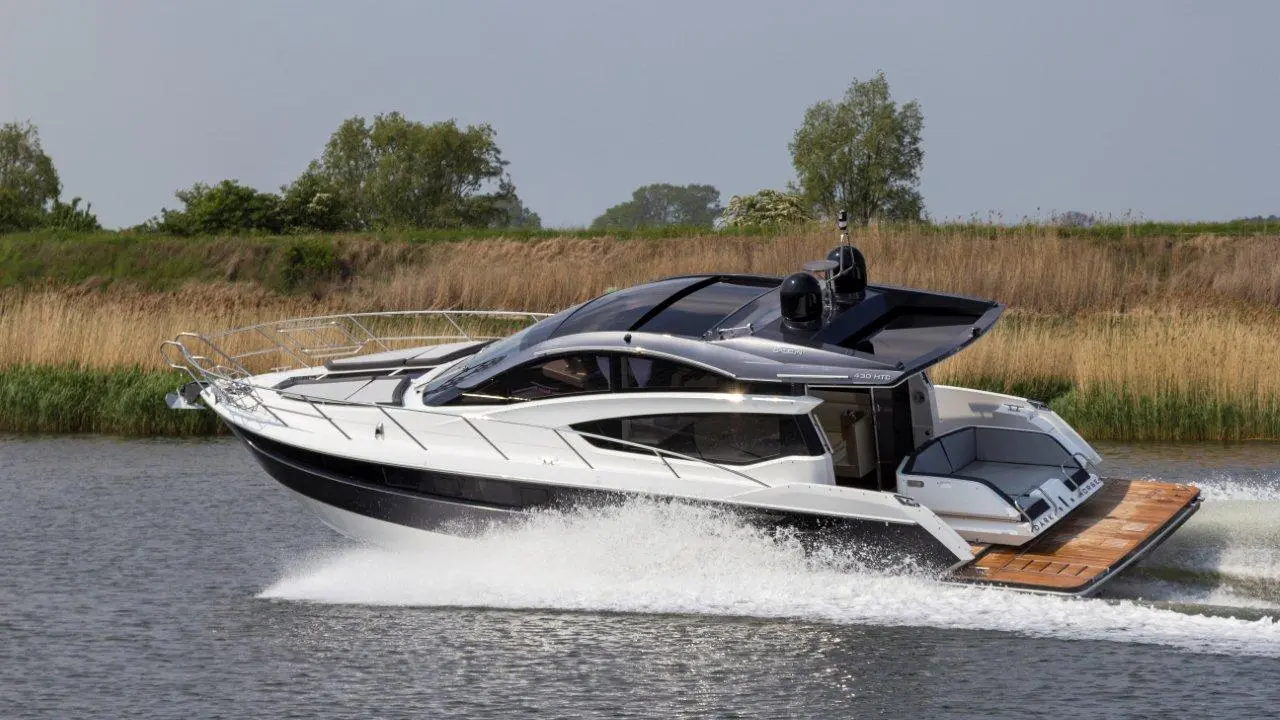 A sleek, motorised luxury yacht speeds through calm waters, showcasing a modern design with panoramic windows and wood accents.