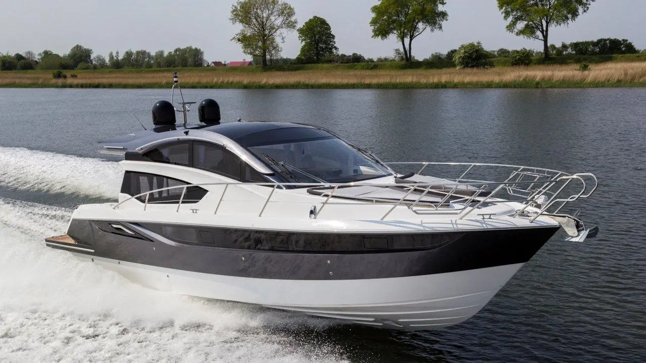 Luxury motor yacht cruising on a river, featuring a sleek design, clear skies, and trees in the background.
