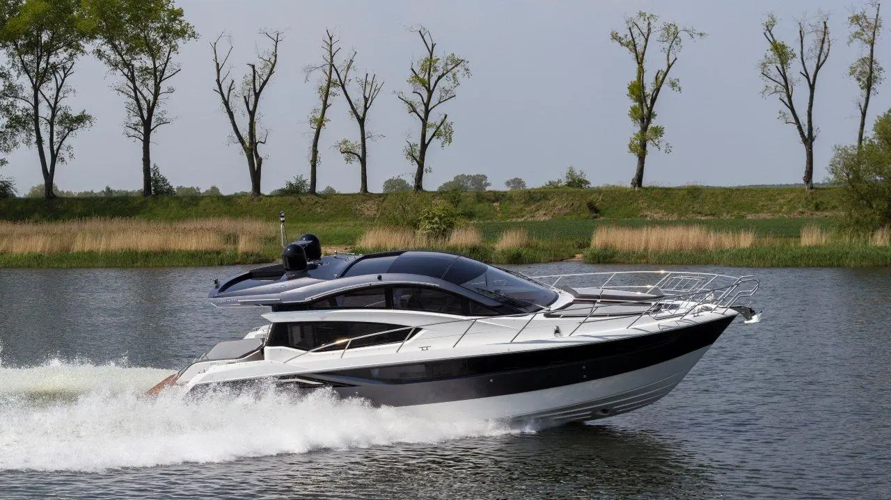 A sleek motorboat glides through calm waters, surrounded by trees and lush green banks, creating a serene outdoor setting.