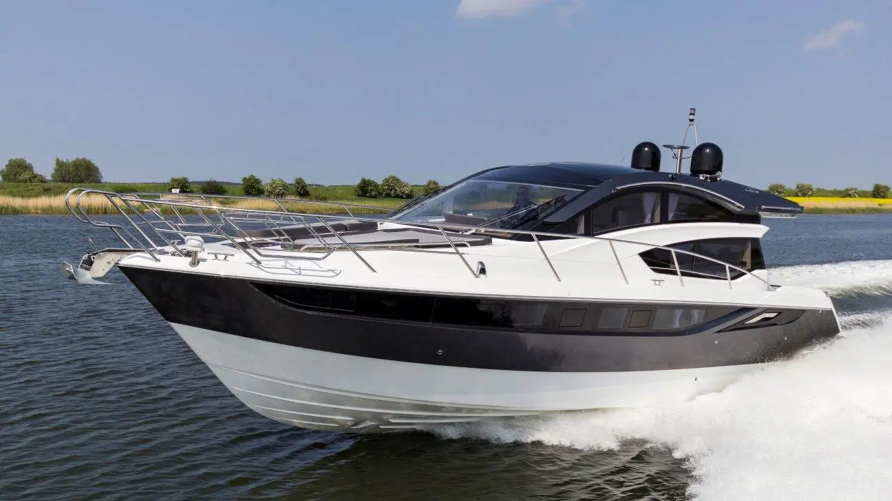 A sleek black and white motorboat cruising on a calm river, surrounded by green vegetation and blue skies.