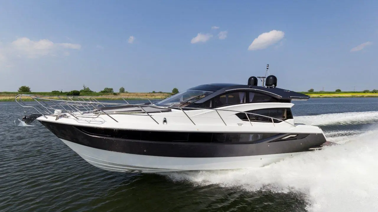 A sleek motorboat glides through calm waters, showcasing a glossy black and white design under a clear blue sky.