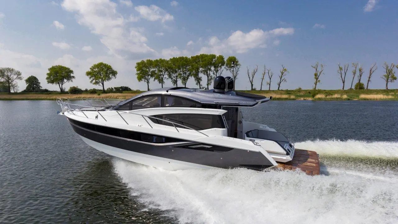 A sleek motorboat glides across a calm waterway, surrounded by green trees and a clear blue sky.