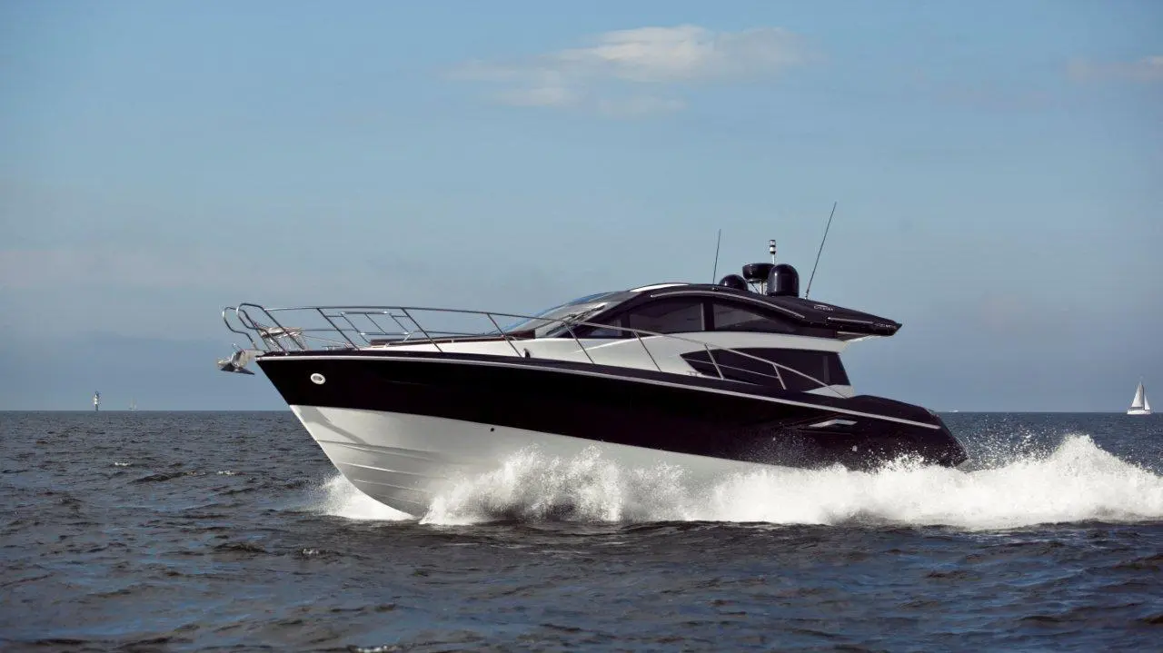 A sleek black and white motorboat accelerates through calm waters under a clear blue sky.