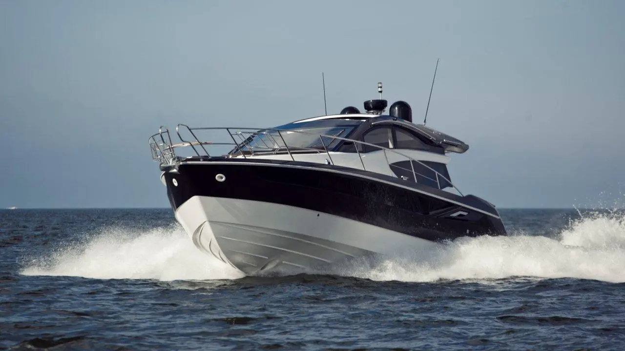 A sleek black and white motorboat speeds through calm waters, creating splashes under a clear sky.