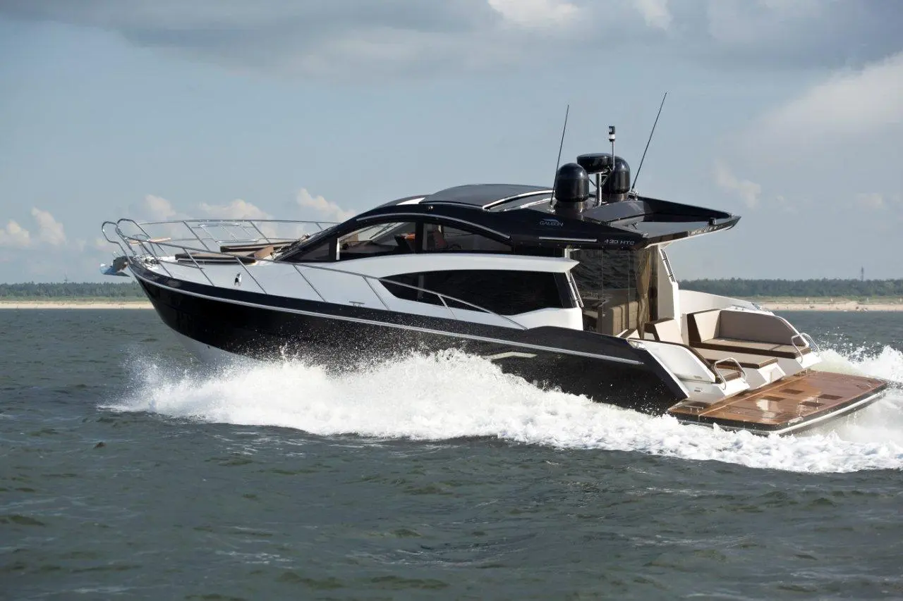 A sleek black and white motor yacht cruising on water, creating waves, with a modern design and spacious deck.