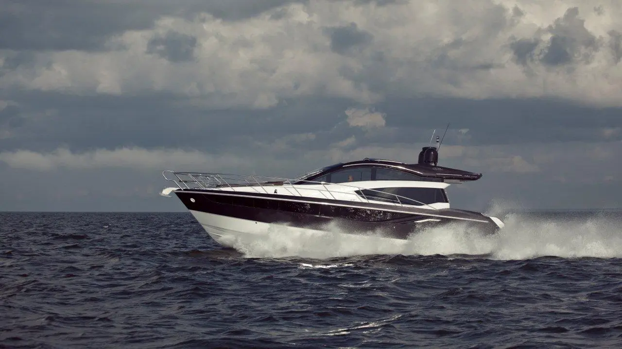 Sleek black and white motor yacht cruising through choppy waters under a cloudy sky, creating splashes behind it.