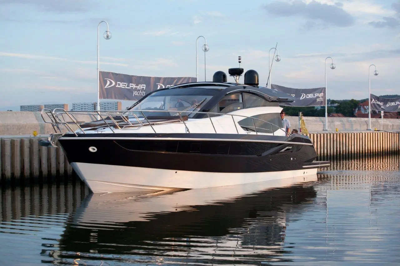 A sleek black and white yacht docked in calm waters with 'Delphia Yachts' banners and a person on board.