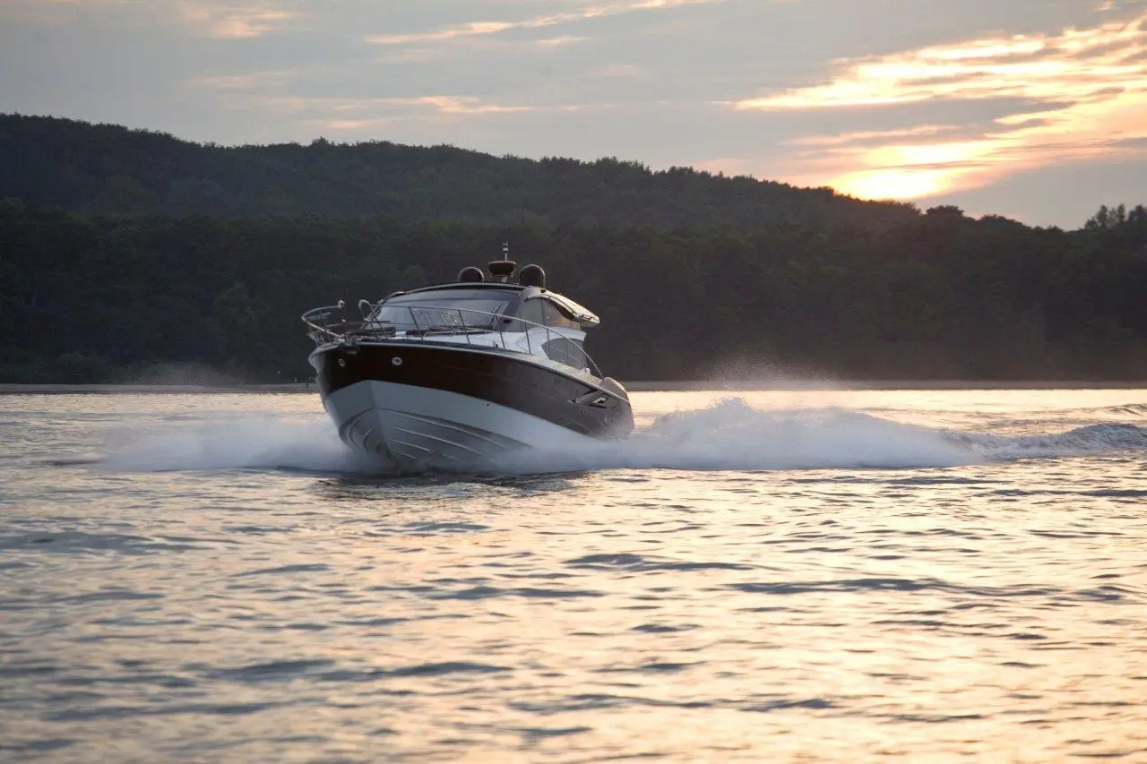 A sleek motorboat glides across the water at sunset, creating splashes and reflecting light from the serene landscape.