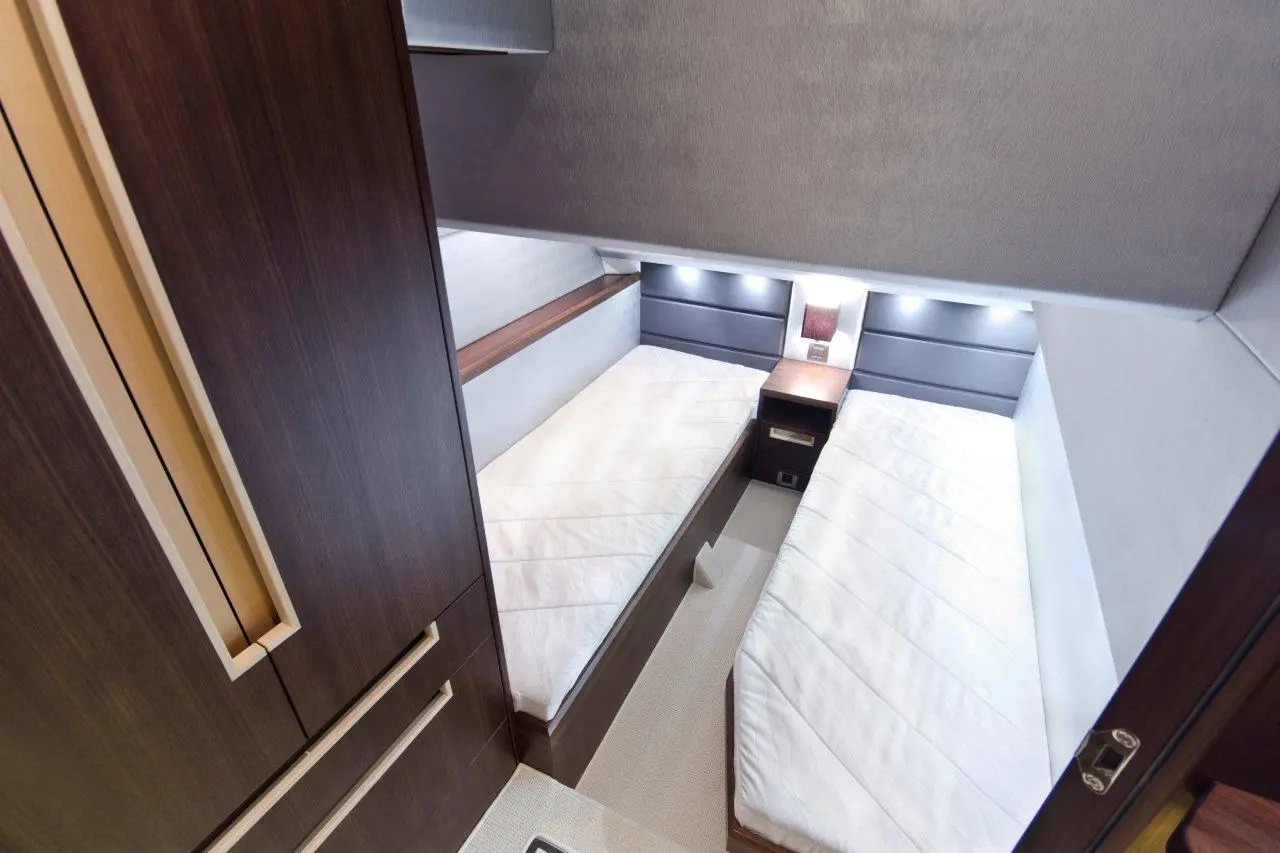 Modern bedroom with two single beds, bedside table, and built-in wardrobe, featuring sleek wooden finishes and soft lighting.