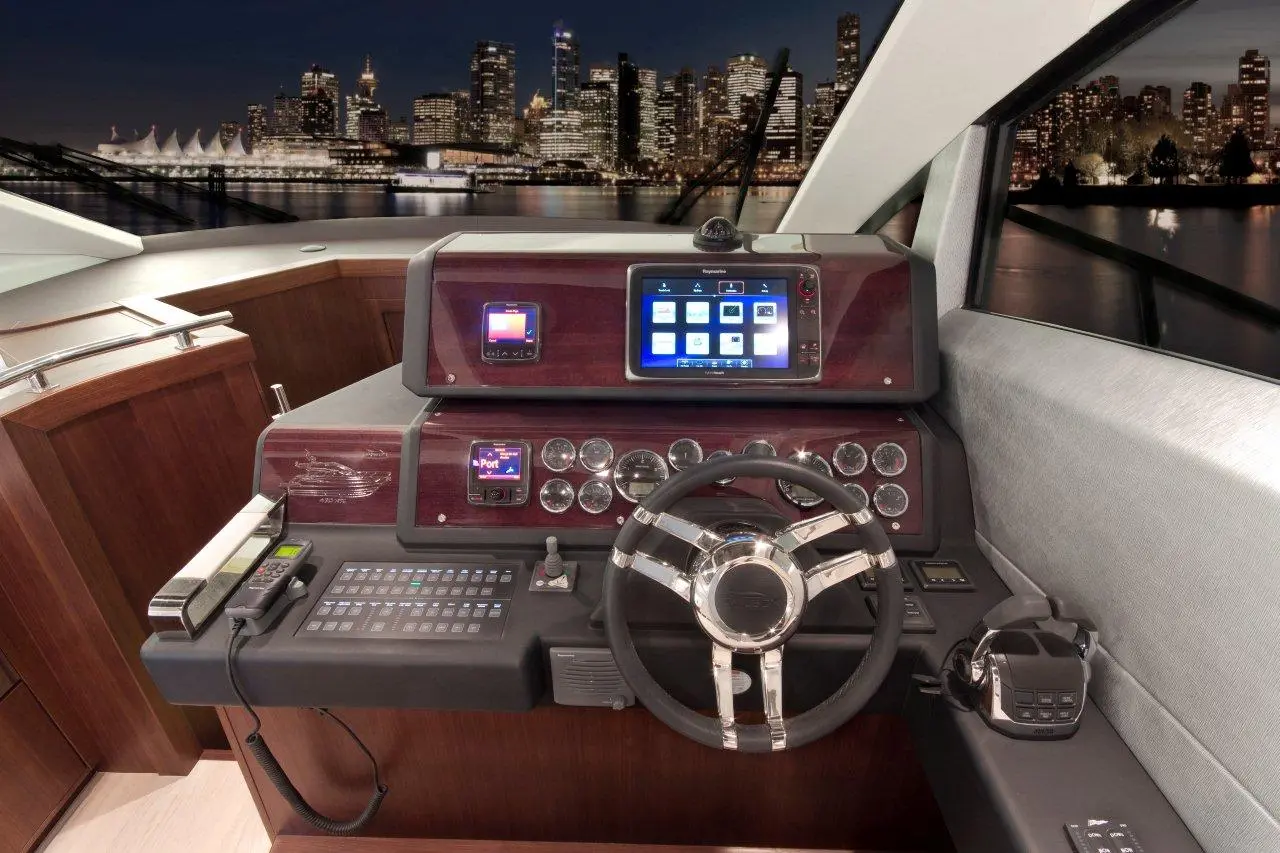 Luxury yacht control panel at night, featuring a steering wheel, digital displays, and city skyline in the background.