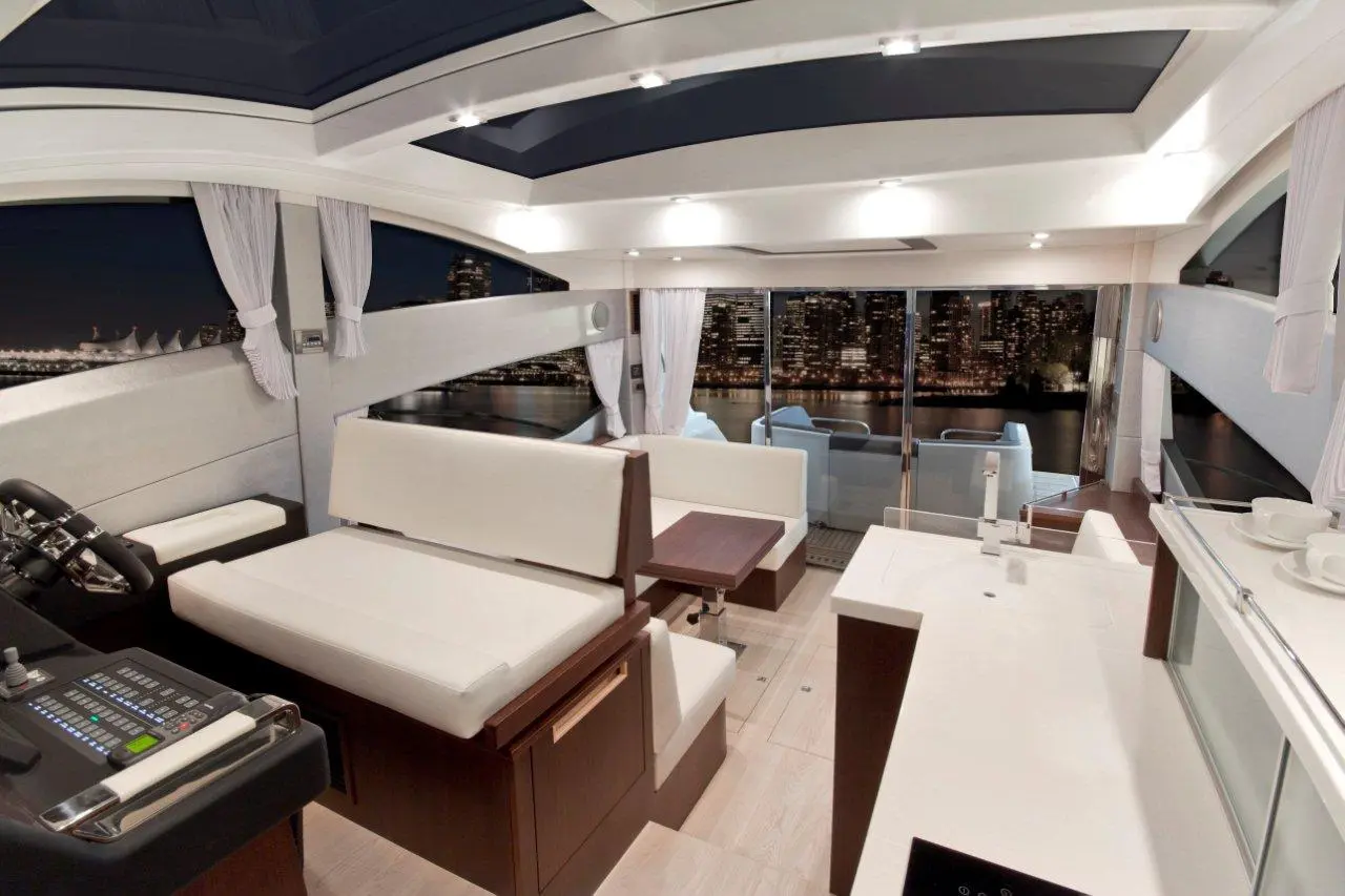 Sleek yacht interior featuring white seating, a wooden table, panoramic city views, and modern controls at night.