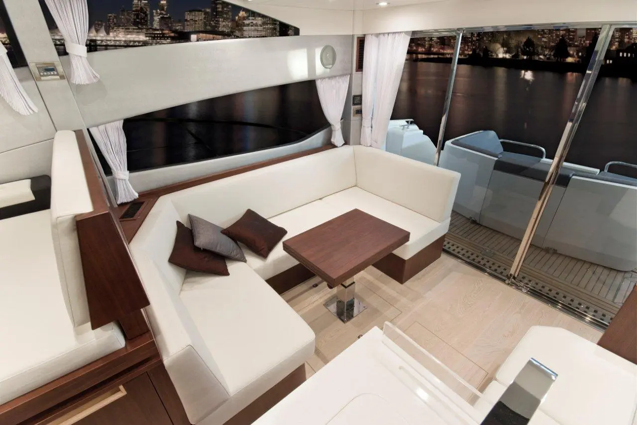 Modern yacht interior with white furnishings, brown cushions, and a view of city lights reflected on water.