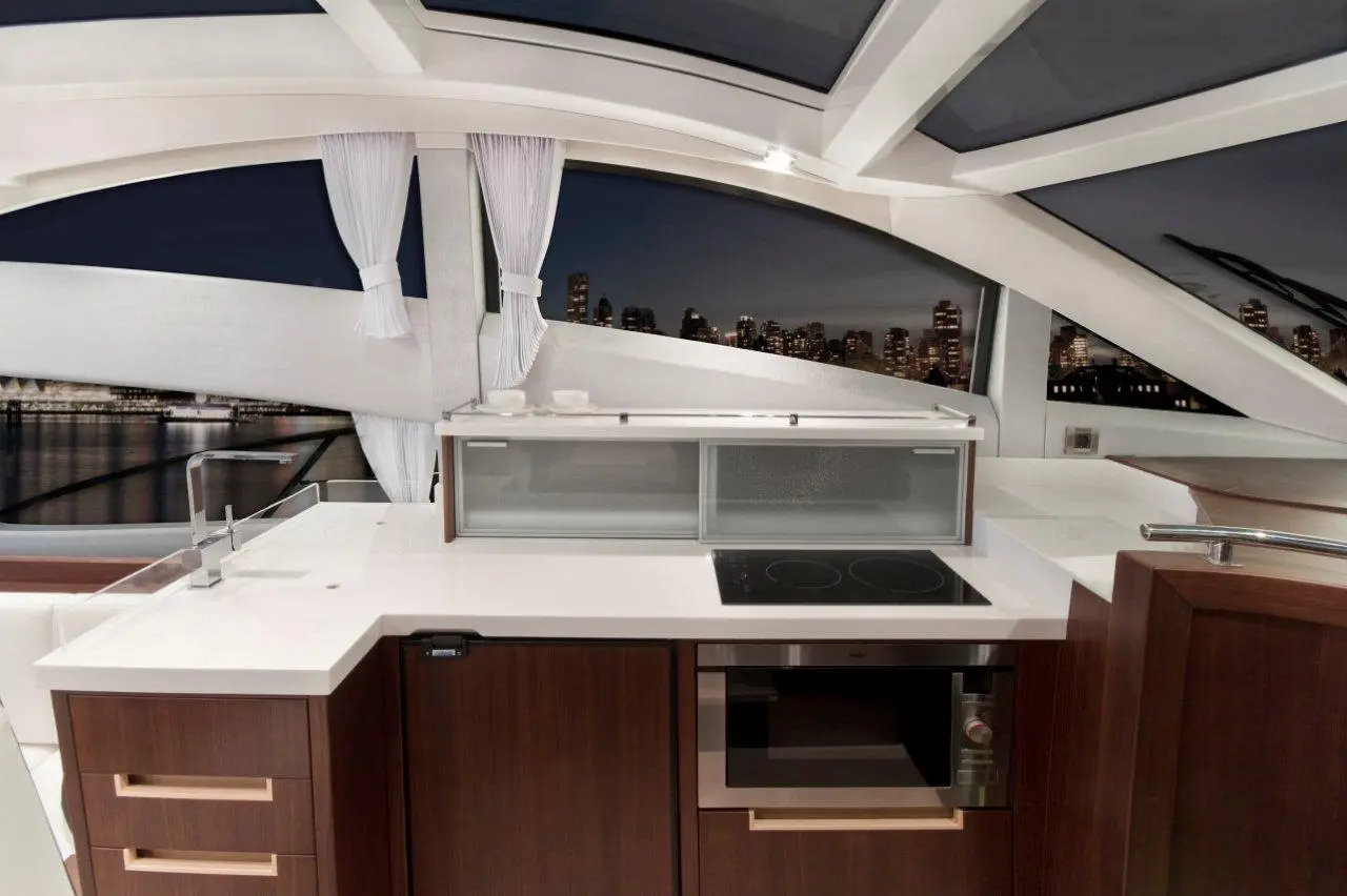 Modern yacht kitchen with white countertops, cooktop, and scenic city skyline view through large windows.