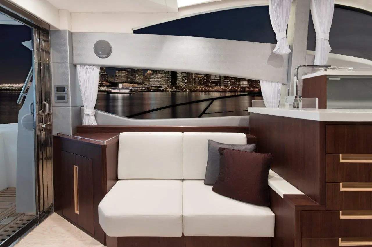 Stylish boat interior featuring a white sofa, dark wood cabinets, and a view of city lights through large windows at night.