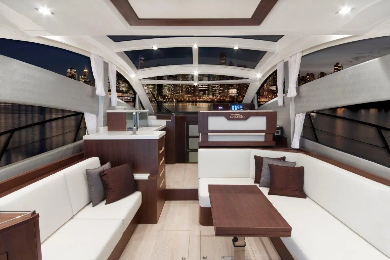Modern yacht interior with white seating, wooden accents, city skyline visible at night, featuring 'GALEON' branding.