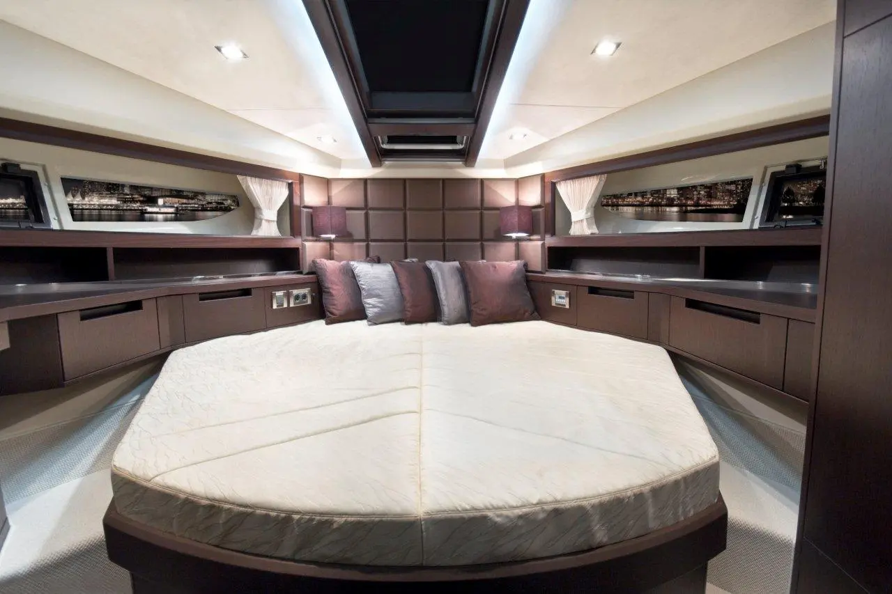 Luxury boat interior featuring a circular bed, dark wood furnishings, decorative cushions, and ambient lighting.