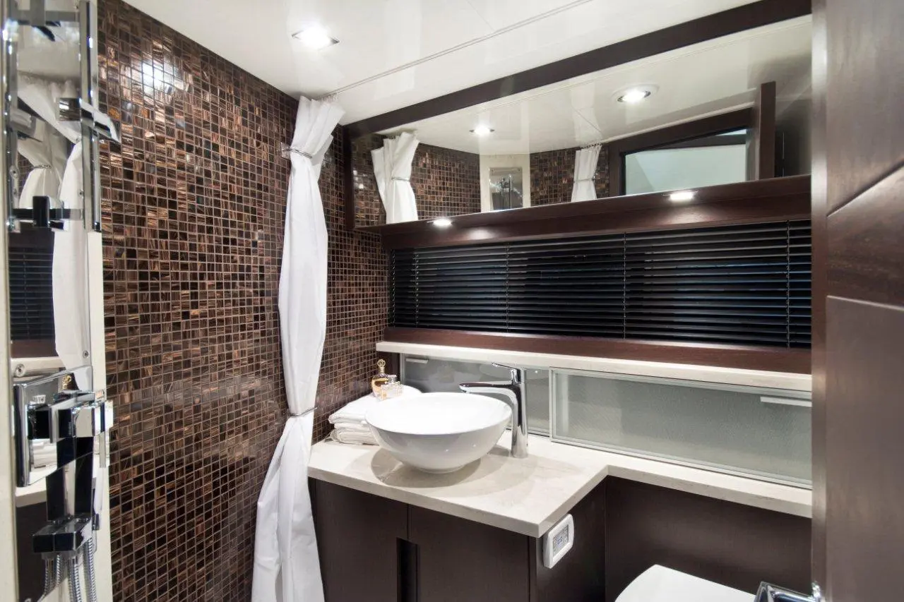 Modern bathroom with brown mosaic tiles, a white bowl sink, countertop, and a large mirror reflecting soft lighting.