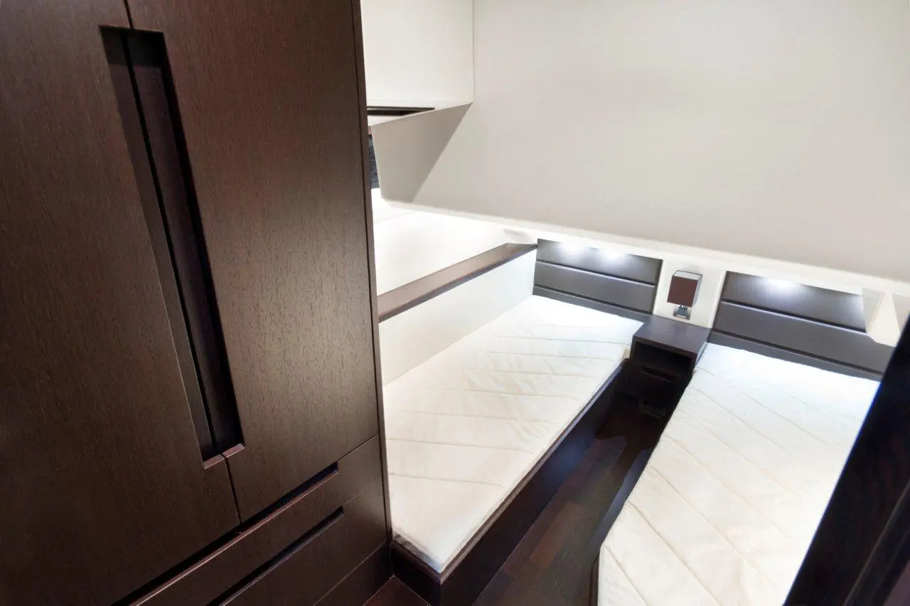Contemporary cabin interior featuring two twin beds, dark wood furniture, and subtle lighting against a white backdrop.