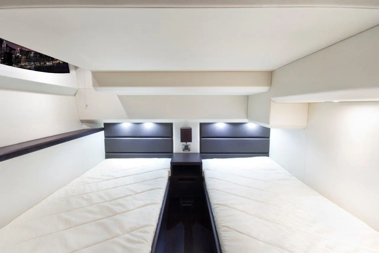 Interior view of a modern cabin with two single beds, fitted with lamps and a window displaying a city skyline.