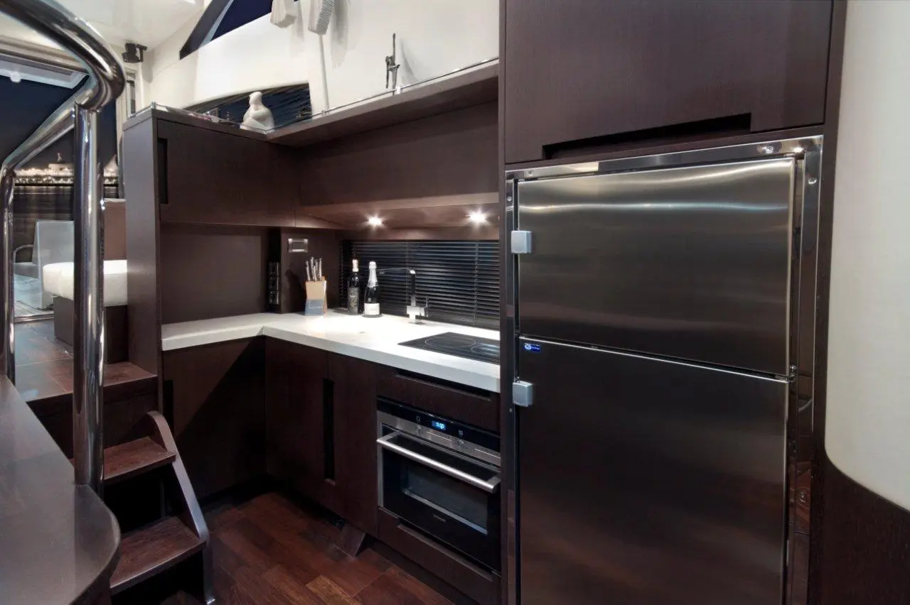 Modern yacht kitchen with dark wood cabinetry, stainless steel fridge, stove, and under-cabinet lighting. Elegant design features.