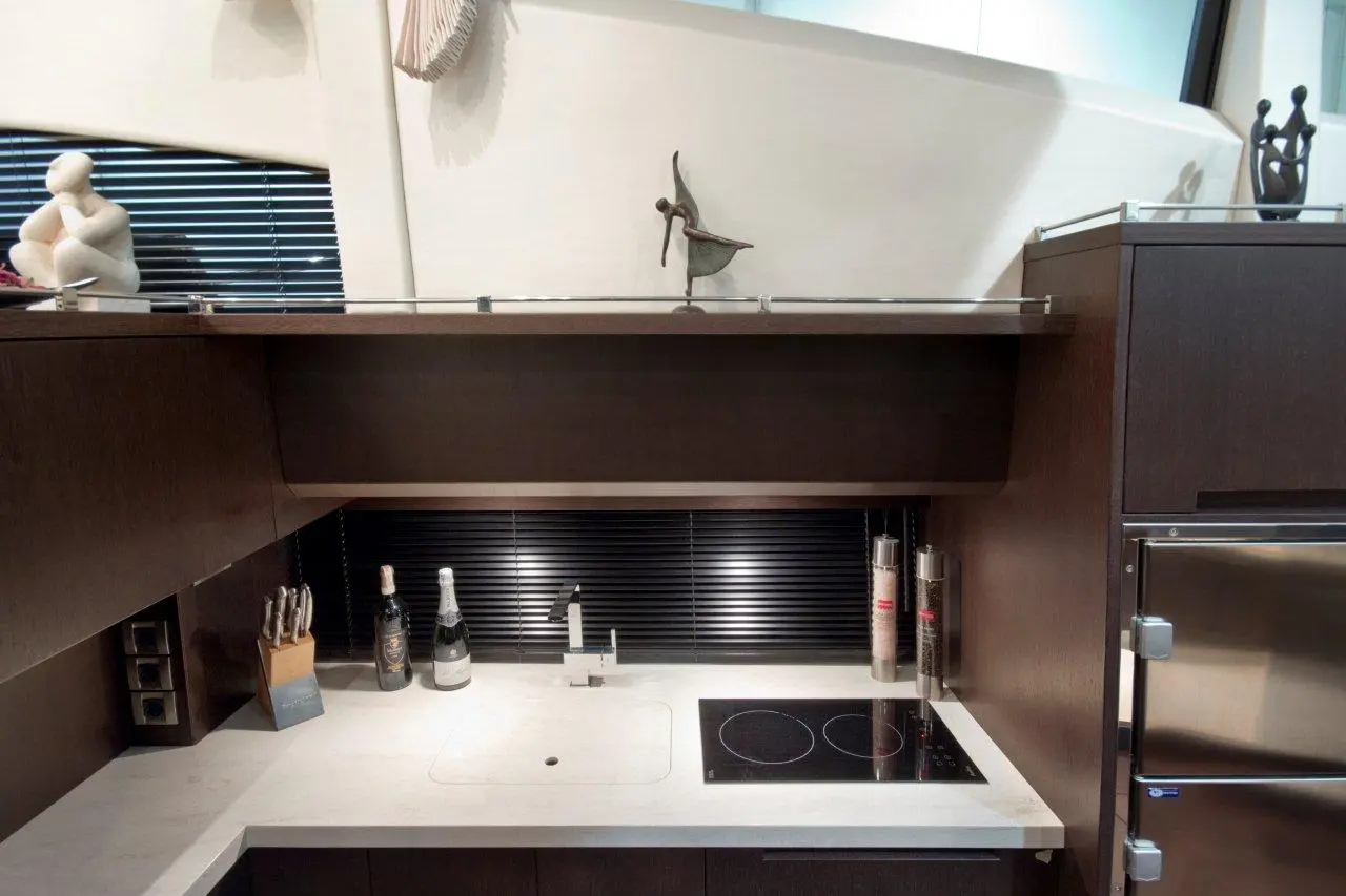 Modern kitchen featuring a minimalist design, with utensils, wine bottles, a sink, and an induction cooktop on marble countertops.