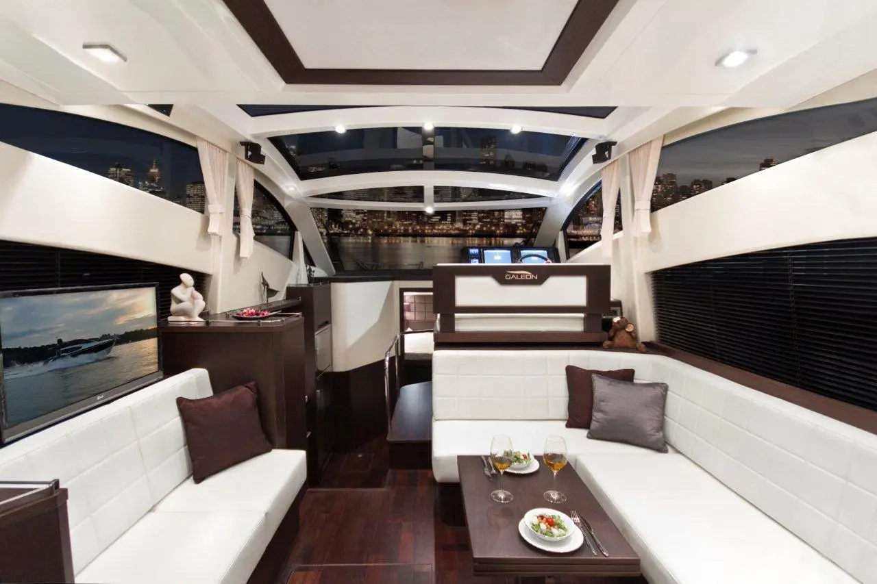 Luxury yacht interior featuring a dining area, white leather seating, elegant decor, and city skyline view through large windows.