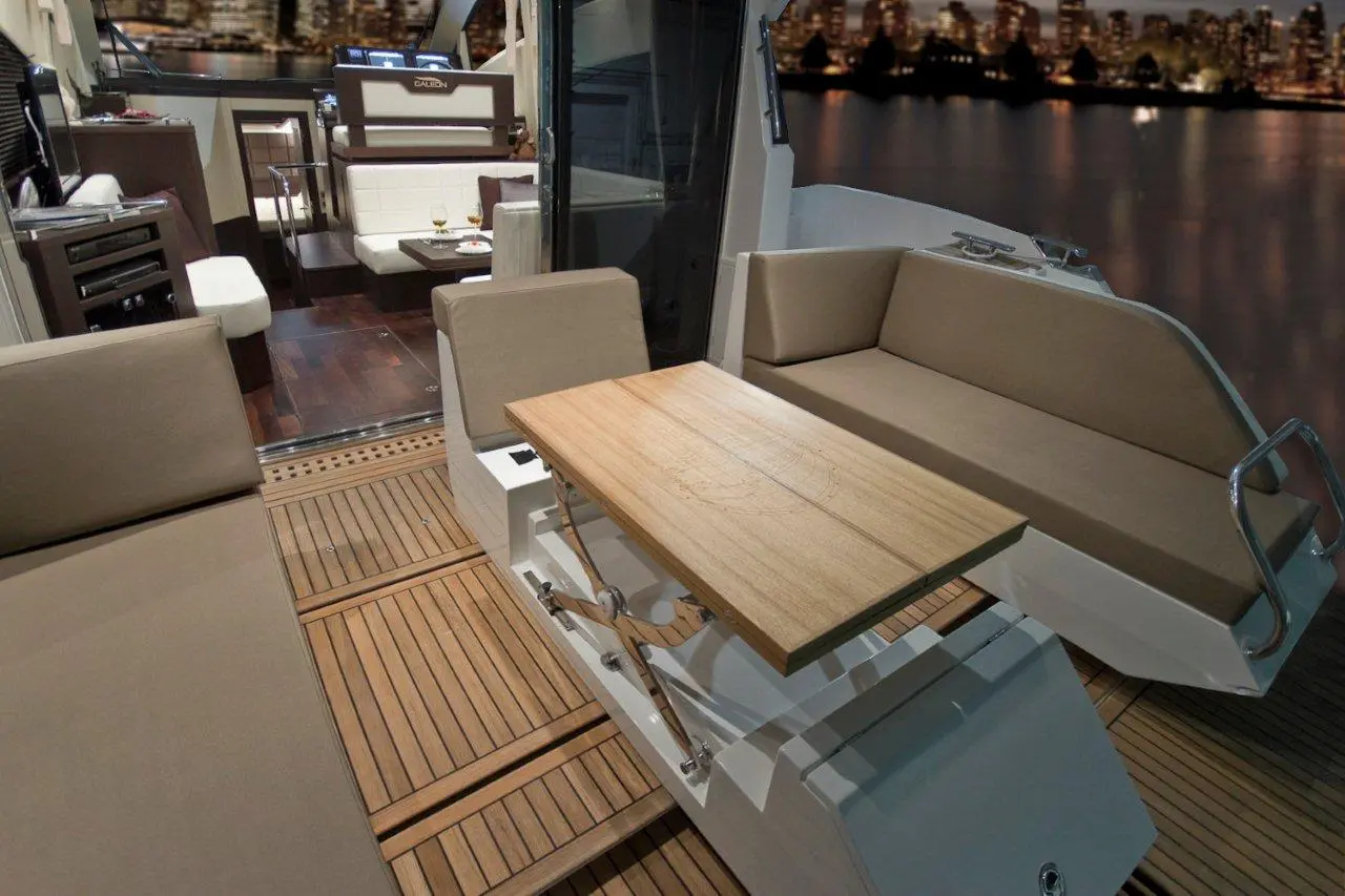 Luxury yacht interior featuring modern seating, a wooden table, and a scenic city skyline view at dusk.