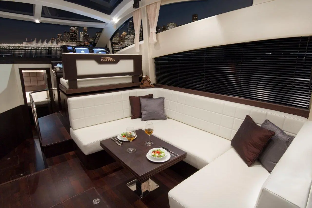 Luxurious yacht interior with white leather seating, a wooden table with food, glasses of drink, and city skyline views.