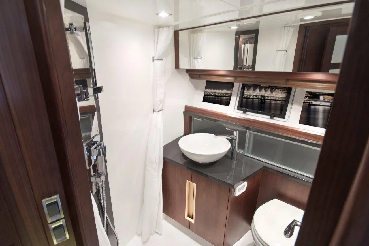 Modern boat bathroom featuring a white bowl sink, wood cabinetry, glass shelves, and mirror with nightscape artwork.
