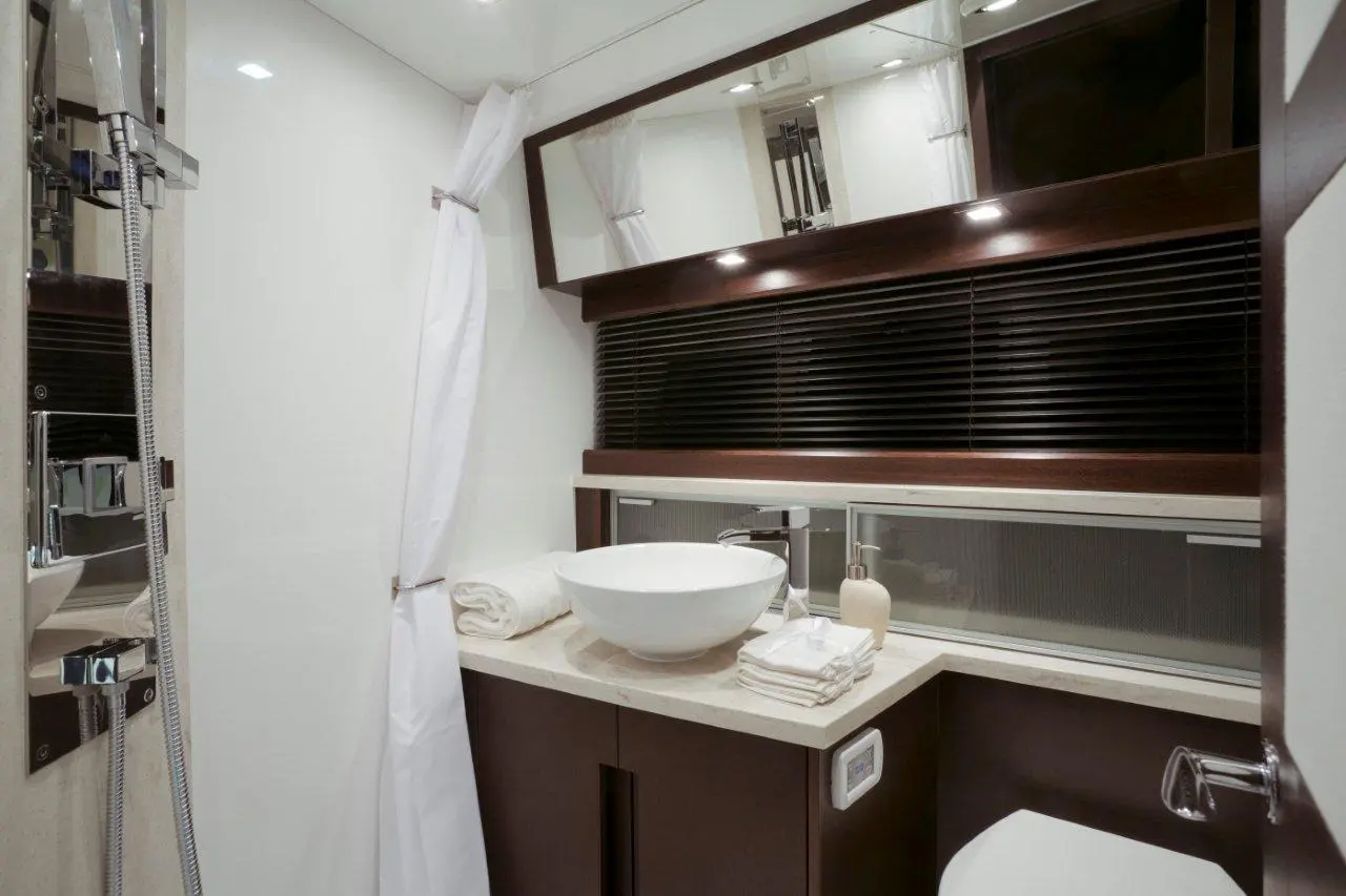Modern bathroom featuring a round basin, towels, soap dispenser, and a shower area with glass partitions and stylish wooden accents.