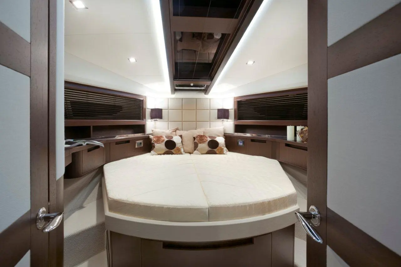 Luxury yacht cabin featuring a round bed, decorative pillows, ambient lighting, and modern wooden cabinetry.