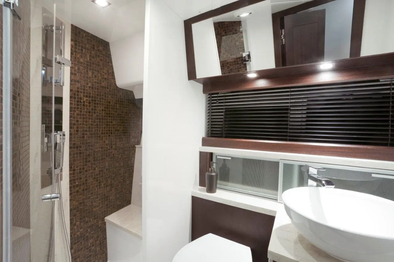 Modern bathroom featuring a shower, sleek sink, wooden accents, and textured wall tiles. Minimalist design and lighting.